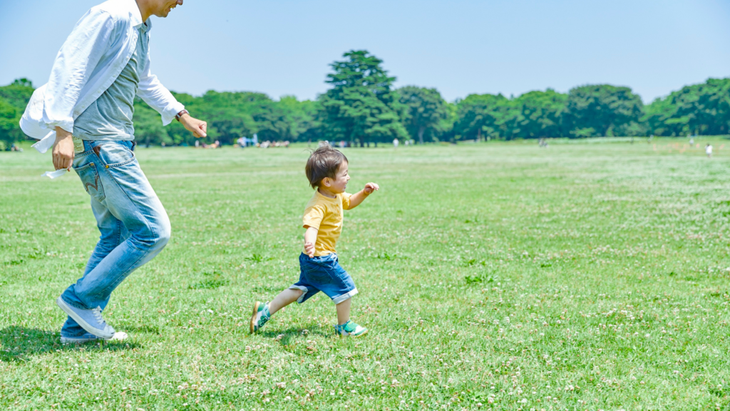 公園の芝生で走って遊ぶ親子(体を使ったフィジカルな時間)